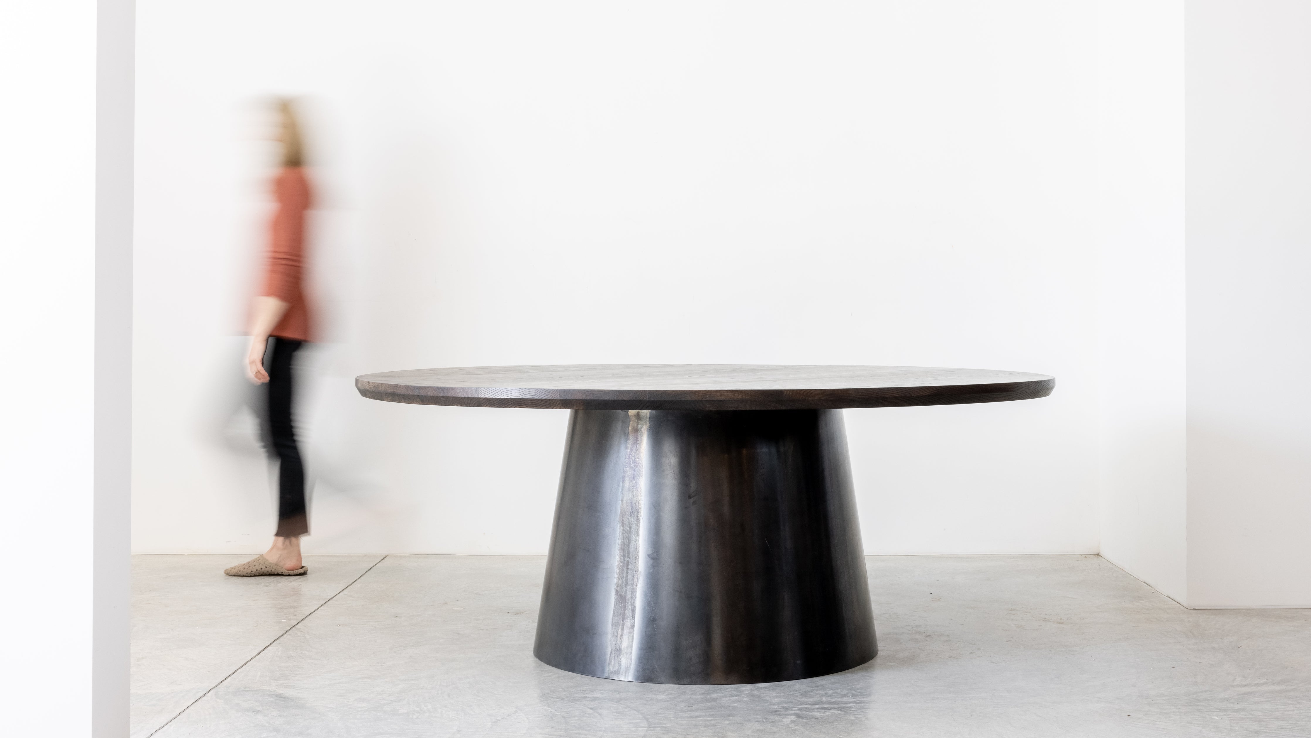 Large round solid wood dining table in a minimalistic room with a blurred person in the background